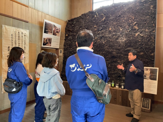 【豊島のこころ資料館】産廃（シュレッダーダスト）の剥ぎ取り壁面の前で説明を受ける様子